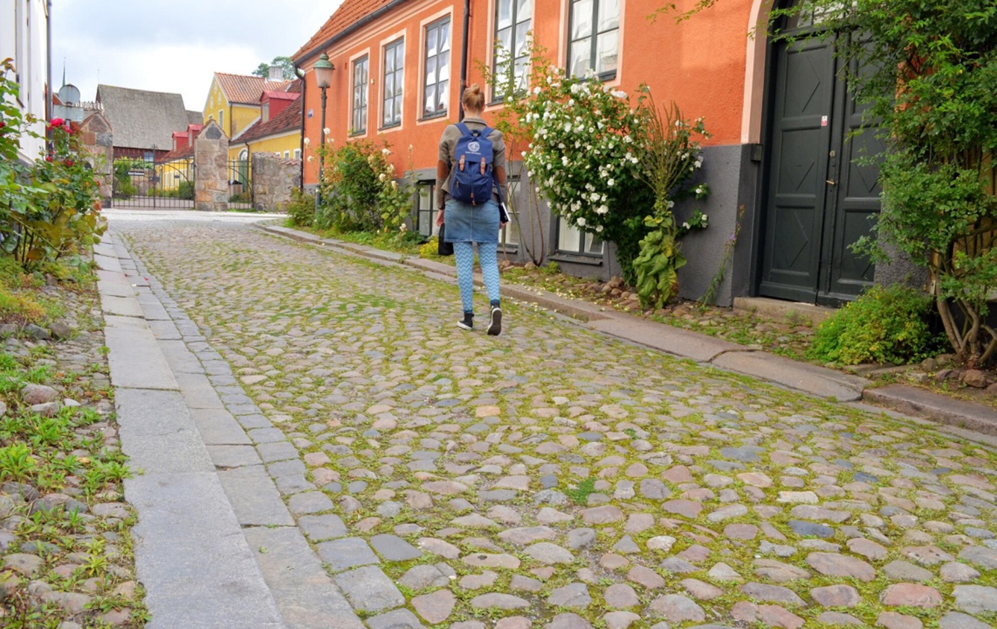 Student walking on cobblestones with a book in one hand